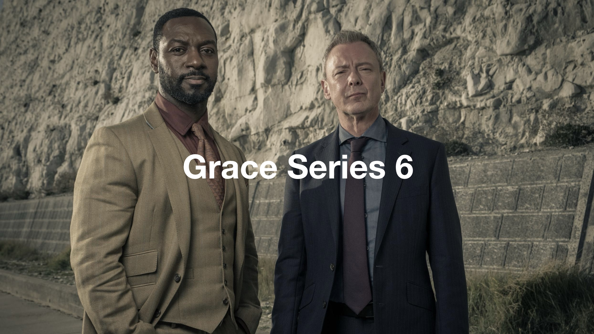 Two male characters standing in front of a rocky wall, dressed in formal suits